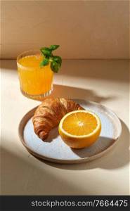 food and eating concept - glass of orange juice with peppermint and croissant on plate for breakfast. glass of orange juice and croissant on plate
