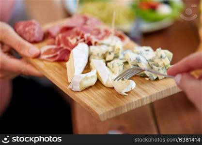 food and eating concept - hands with blue cheese and jamon or parma ham on wooden board. hands with blue cheese and jamon or ham on board