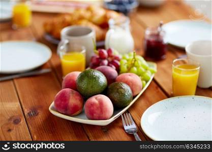 food and eating concept - plate of fruits, orange juice, milk and jam on wooden table at breakfast. fruits, juice and other food on table at breakfast