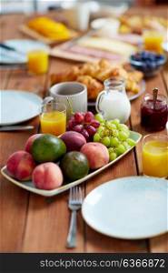 food and eating concept - plate of fruits, orange juice, milk and jam on wooden table at breakfast. fruits, juice and other food on table at breakfast