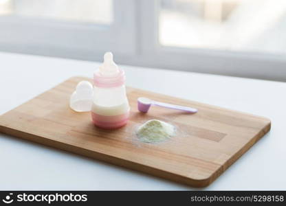 food and nutrition concept - infant formula milk powder, baby bottle and scoop on wooden cutting board. infant formula, baby bottle and scoop on board