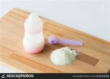 food and nutrition concept - infant formula milk powder, baby bottle and scoop on wooden cutting board. infant formula, baby bottle and scoop on board