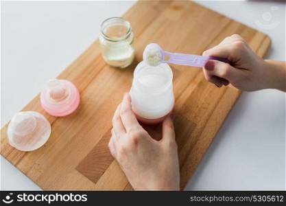 food and nutrition concept - mother hands with baby bottle and scoop preparing infant formula milk. hands with bottle and scoop making formula milk