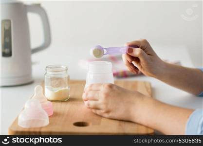 food and nutrition concept - mother hands with baby bottle and scoop preparing infant formula milk. hands with bottle and scoop making formula milk