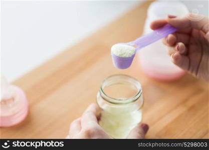 food and nutrition concept - mother hands with jar, scoop and baby bottle preparing infant formula milk. hands with jar and scoop making formula milk