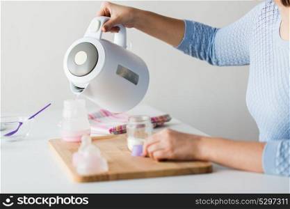 food and nutrition concept - mother hands with kettle pouting boiled water to baby bottle and making infant formula milk. hands with kettle and bottle making baby milk