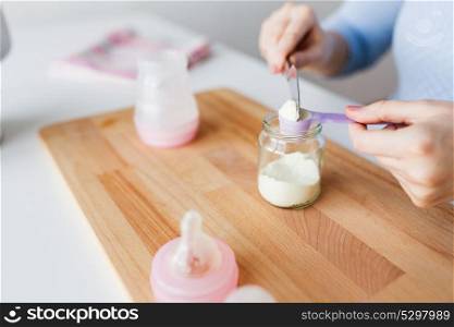 food and nutrition concept - mother hands with scoop, jar and baby bottle preparing infant formula milk. hands with jar and scoop making formula milk