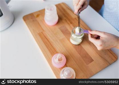 food and nutrition concept - mother hands with scoop, jar and baby bottle preparing infant formula milk. hands with jar and scoop making formula milk