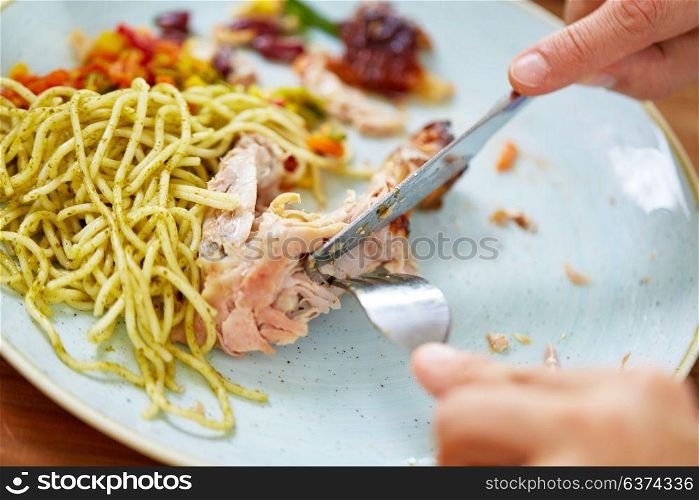 food and people concept - close up of hands with fork and knife eating chicken meat with pasta. close up of hands eating chicken meat with pasta