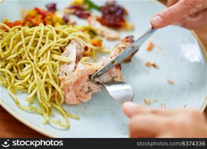 food and people concept - close up of hands with fork and knife eating chicken meat with pasta. close up of hands eating chicken meat with pasta