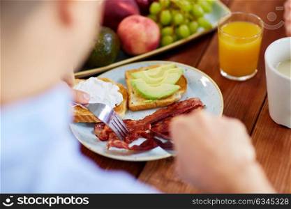 food and people concept - hands of man eating toast with mozzarella, egg and bacon with fork and knife. man eating toast with mozzarella, egg and bacon