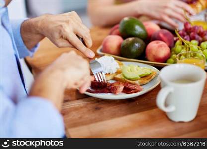 food and people concept - hands of man with fork eating bacon at table. man with fork eating bacon at table full of food