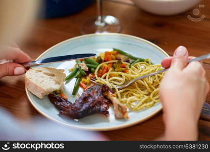 food and people concept - hands of woman with fork and knife eating pasta and roast chicken at wooden table. hands of woman eating pasta and roast chicken