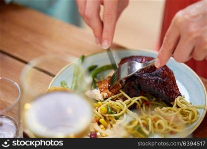 food and people concept - hands of woman with fork eating roast chicken at wooden table. hands of woman with fork eating roast chicken