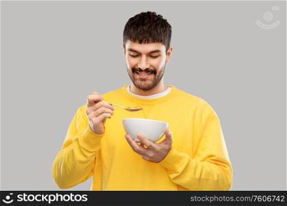 food and people concept - happy smiling young man eating cereals over grey background. happy smiling young man eating cereals