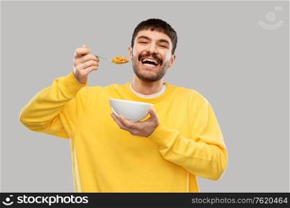 food and people concept - happy smiling young man eating cereals over grey background. happy smiling young man eating cereals