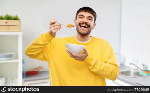 food and people concept - happy smiling young man eating cereals over home kitchen background. happy smiling young man eating cereals