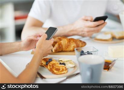 food and technology concept - close up of couple with smartphones having breakfast at home. close up of couple with smartphones at breakfast