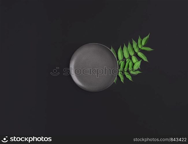 Food backdrop with empty grey plate and green leaves ornament on a black table. Above view of minimal style table settings. Mockup tableware for food