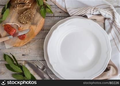 Food background. Empty plate, cutlery, chorizo sausage, bread and laurel and kitchen towel on wooden table