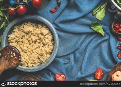 Food background for Quinoa recipes and cooking. Cooked quinoa with wooden spoon and vegetables ingredients on dark blue background, top view, place for text. Superfood concept.