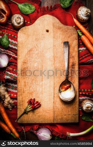 Food background for traditional national cuisine with aged cutting board, vegetables, cooking spoon and red country tablecloth with embroidery, top view, frame