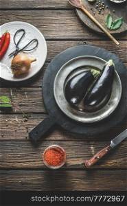 Food background with eggplant on plate and cutting board with herbs. Healthy ingredients and kitchen utensils on rustic wooden kitchen table. Cooking preparation. Top view.