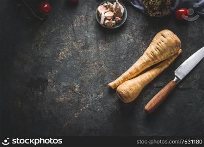 Food background with fresh parsnips roots on dark kitchen tables with knife. Top view. Vegetables cooking concept