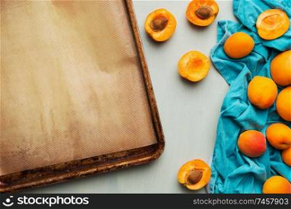 Food background with fresh whole and halved apricot bunch and empty baking sheet, top view. Seasonal fruits concept.
