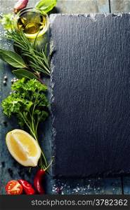 Food background, with herbs, spices, olive oil, salt, lemons and vegetables. Slate and wood background.