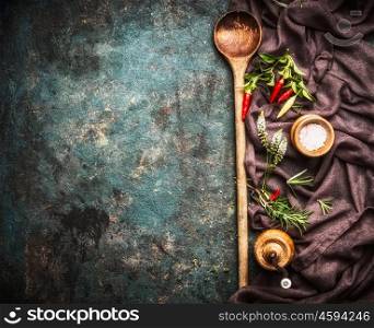 Food background with old wooden cooking spoon , napkin , spices and flavoring on dark rustic background, top view, border