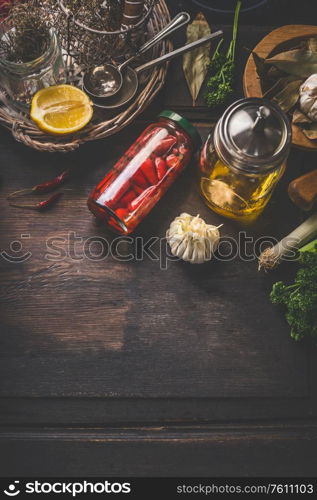 Food background with pickled vegetables, jar with olives oil, herbs and spices on dark kitchen table. Top view. Home cuisine. Tasty cooking and preserving