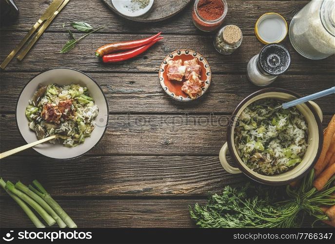 Food background with rice dish in bowl with leek and meat, vegetables, chili pepper, herbs, spices, cutlery and kitchen utensils at rustic brown wooden table. Cooking healthy food. Top view.