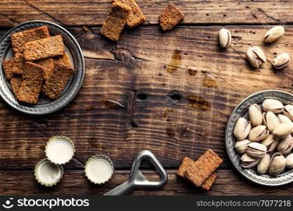 food background with salty snacks and beer bottle caps on old brown wooden table top with space for your text, beer party concept