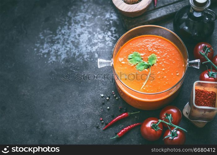 Food background with tomato soup or sauce in glass cooking pot on dark table with ingredients, top view. Copy space. Homemade healthy eating and cooking. Vegetarian food.