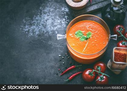 Food background with tomato soup or sauce in glass cooking pot on dark table with ingredients, top view. Copy space. Homemade healthy eating and cooking. Vegetarian food.
