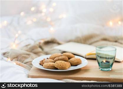 food, bakery and hygge concept - oatmeal cookies on plate and candle in holder at home. oatmeal cookies and candle in holder at home