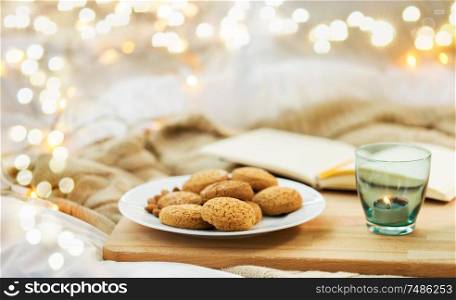 food, bakery and hygge concept - oatmeal cookies on plate and candle in holder at home. oatmeal cookies and candle in holder at home