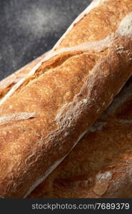 food, baking and cooking concept - close up of baguette bread on table over dark background. close up of baguette bread on kitchen towel