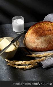 food, baking and cooking concept - close up of bread, butter in bowl, knife and glass of milk on kitchen table. close up of bread, butter, knife and glass of milk