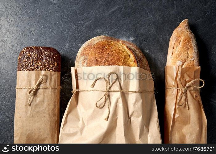 food, baking and cooking concept - close up of bread in paper bags on table over dark background. close up of bread in paper bags on table