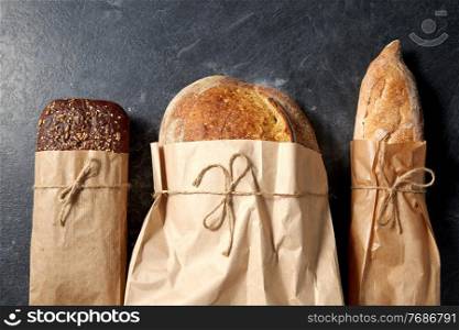 food, baking and cooking concept - close up of bread in paper bags on table over dark background. close up of bread in paper bags on table