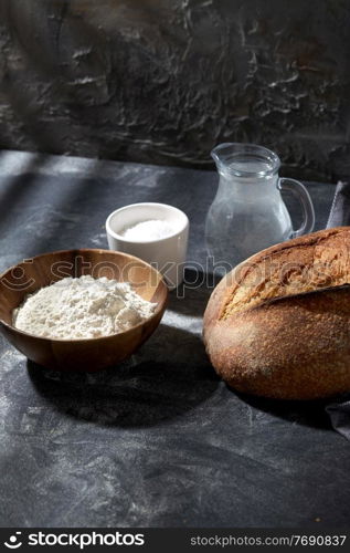 food, baking and cooking concept - homemade craft bread, wheat flour, salt and water in glass jug on table. bread, wheat flour, salt and water in glass jug