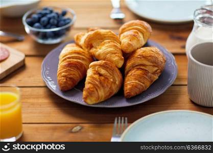 food, baking and eating concept - plate of croissants on wooden table at breakfast. plate of croissants on wooden table at breakfast
