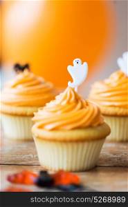 food, baking and holidays concept - cupcake or muffin with halloween party ghost decoration on wooden table. cupcake with halloween decoration