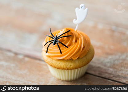 food, baking and holidays concept - cupcake or muffin with halloween party decorations on wooden table. cupcake with halloween decoration on table