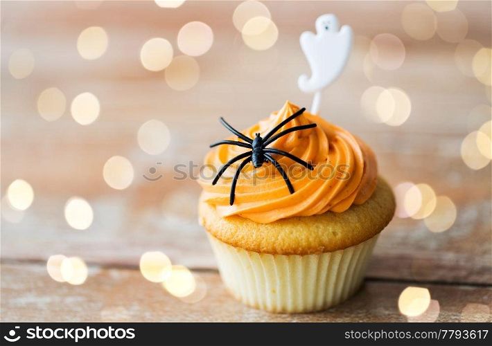 food, baking and holidays concept - cupcake or muffin with halloween party decorations on wooden table. cupcake with halloween decoration on table
