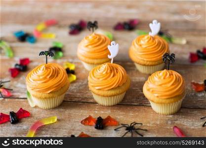 food, baking and holidays concept - cupcakes or frosted muffins with halloween party decorations and candies on wooden table. halloween party decorated cupcakes on wooden table