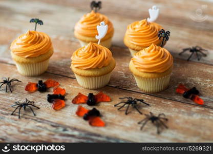 food, baking and holidays concept - cupcakes or frosted muffins with halloween party decorations and candies on wooden table. halloween party decorated cupcakes on wooden table