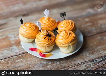 food, baking and holidays concept - cupcakes or muffins and candies with halloween party decorations on wooden table. halloween party cupcakes or muffins on table